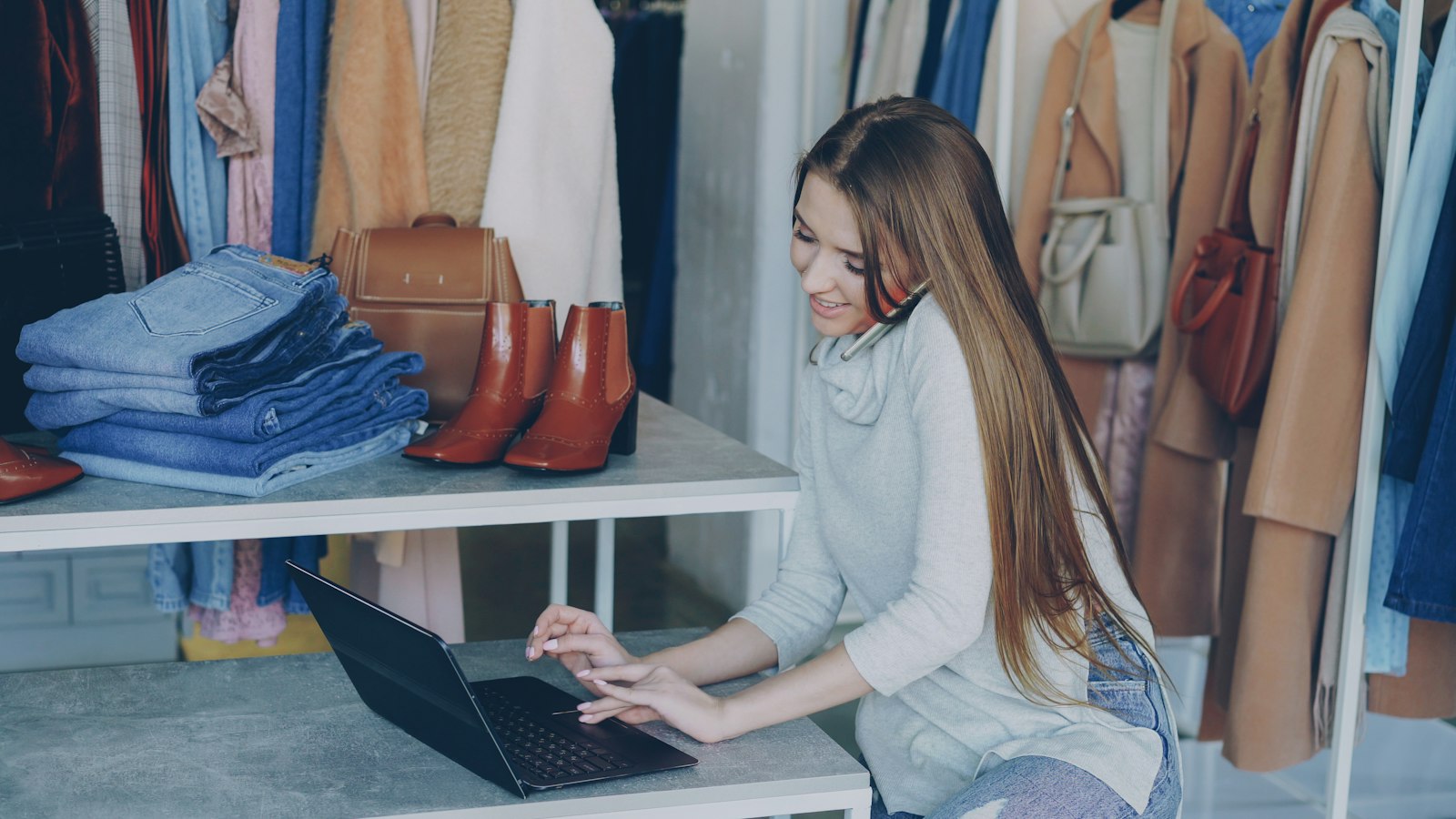 Commerçante dans sa boutique de vêtements, au téléphone devant son ordinateur portable